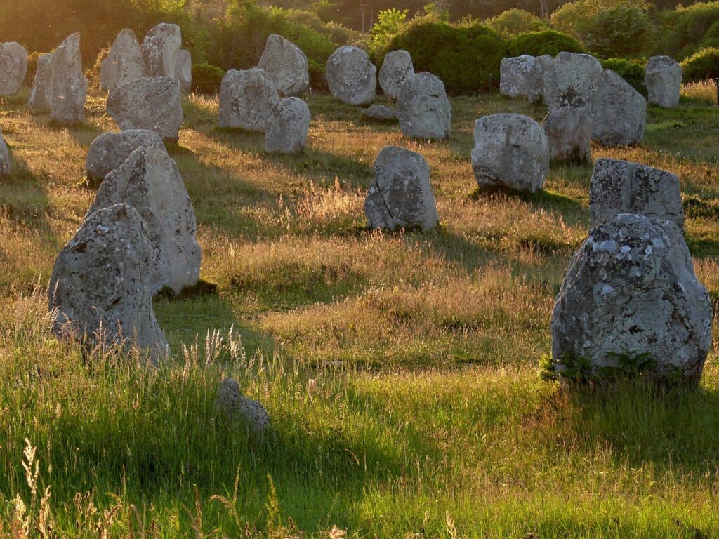 Alignements de menhirs dans un champ au coucher du soleil, symbolisant l’ancrage énergétique des lieux en numérologie.
