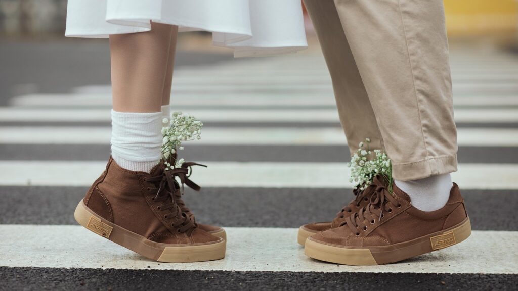Deux personnes face à face, debout sur un passage piéton, portant des chaussures assorties avec des fleurs blanches glissées dans les chaussettes.