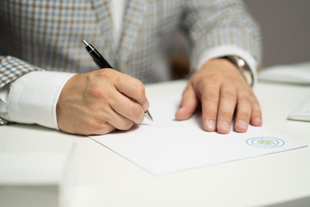 Main d’une personne en train d’écrire sur une feuille blanche, symbole de réflexion, d’analyse et de décision.