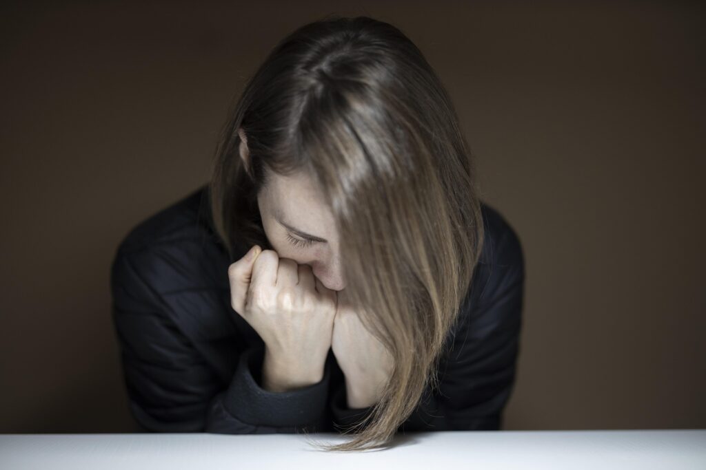 Femme appuyée vers l’avant, la tête baissée, exprimant la fatigue, la tristesse ou la surcharge émotionnelle.
