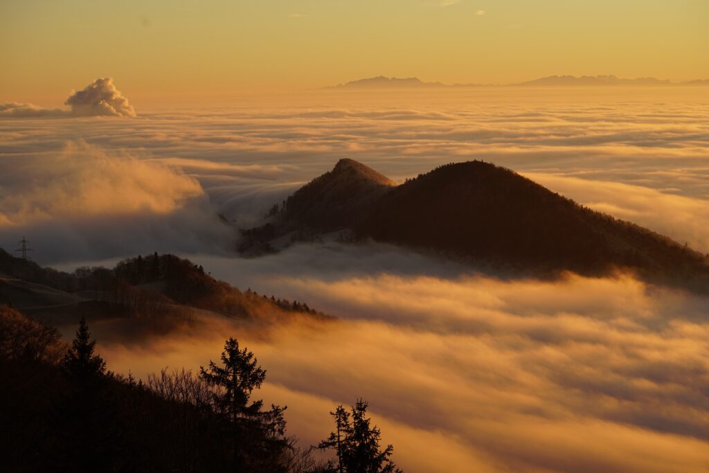 Paysage de montagnes émergeant d’une mer de nuages sous une lumière dorée.
