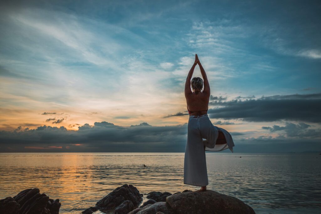 Personne en posture d’équilibre face à la mer au coucher du soleil, illustrant la sensibilité, l’ancrage intérieur et la force relationnelle.