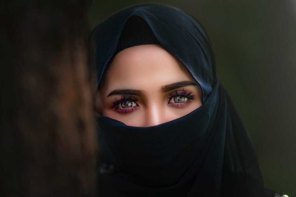 Portrait rapproché d’une femme au regard intense, le visage partiellement couvert, illustrant la présence, l’intensité intérieure et la sensibilité profonde.