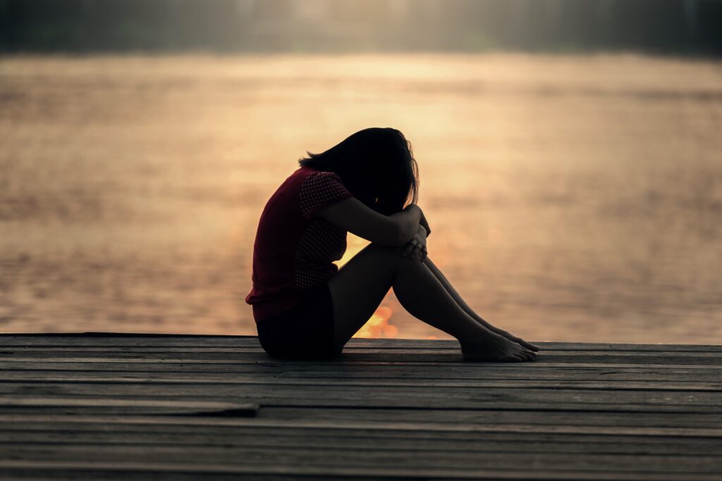 Personne assise seule sur un ponton au bord de l’eau, la tête baissée, dans une ambiance de solitude et de réflexion intérieure.