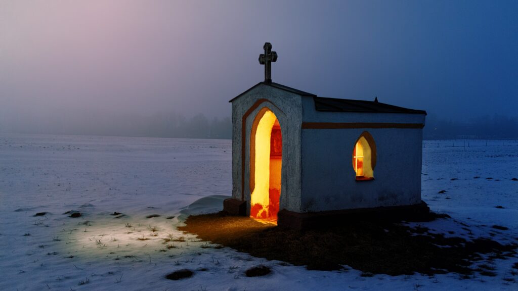 Petite chapelle éclairée au milieu d’un paysage enneigé à la tombée de la nuit.